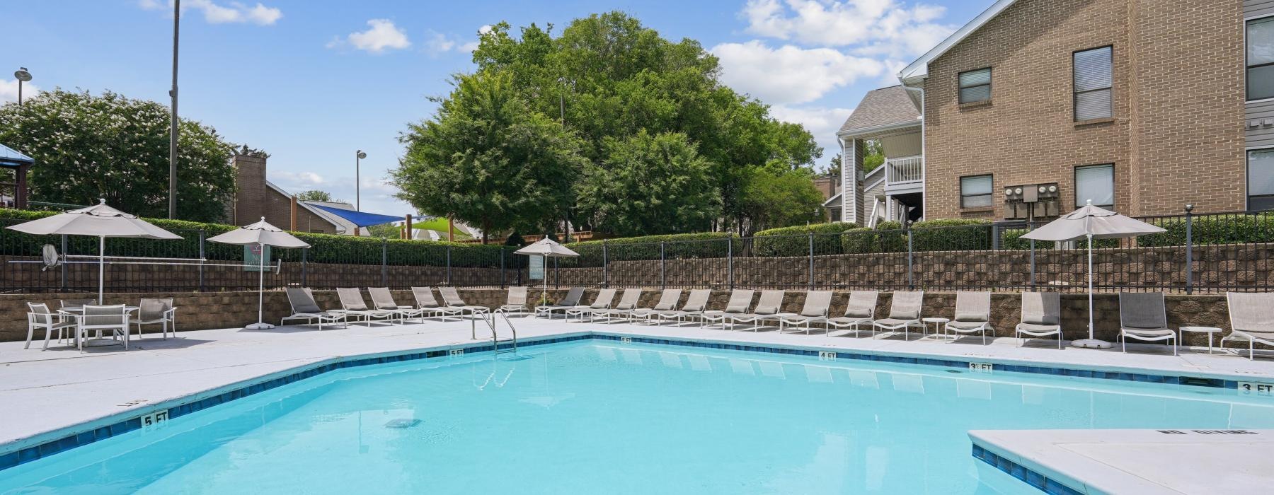 a swimming pool with chairs and umbrellas by a building
